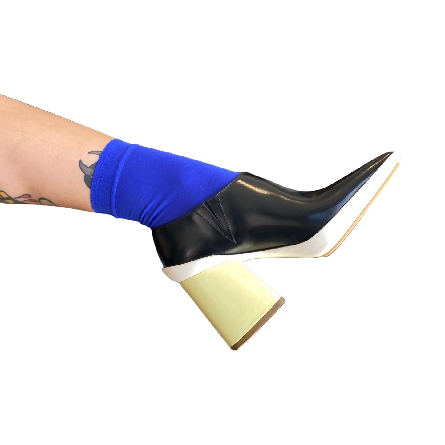 Black high-heeled boot with a white sole worn by a person with blue socks on a black and white background