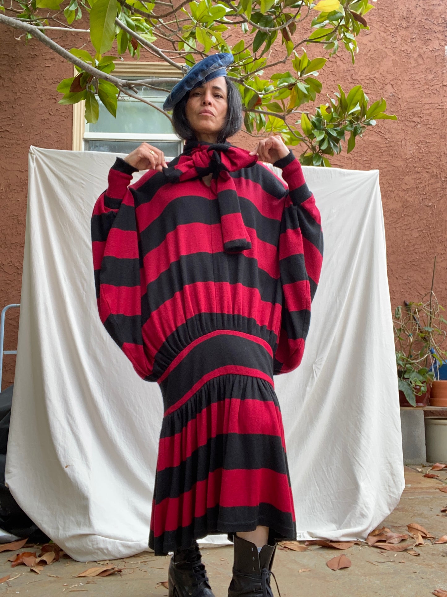 Person wearing a red and black striped outfit standing in front of a white sheet.
