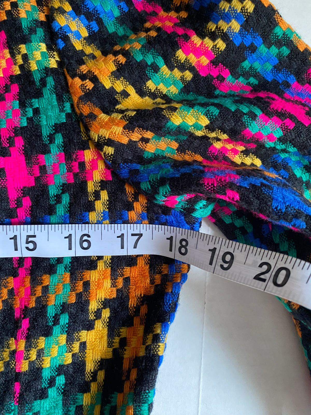 A close-up of a multicolor geometric patterned fabric with a white measuring tape ruler showing the width in inches.