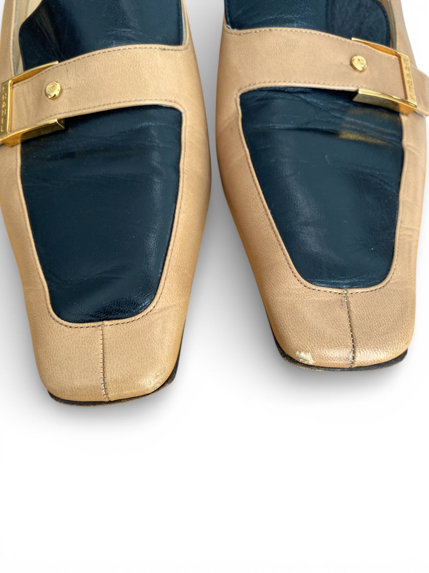 Pair of Chanel beige shoes with gold buckles on a white background