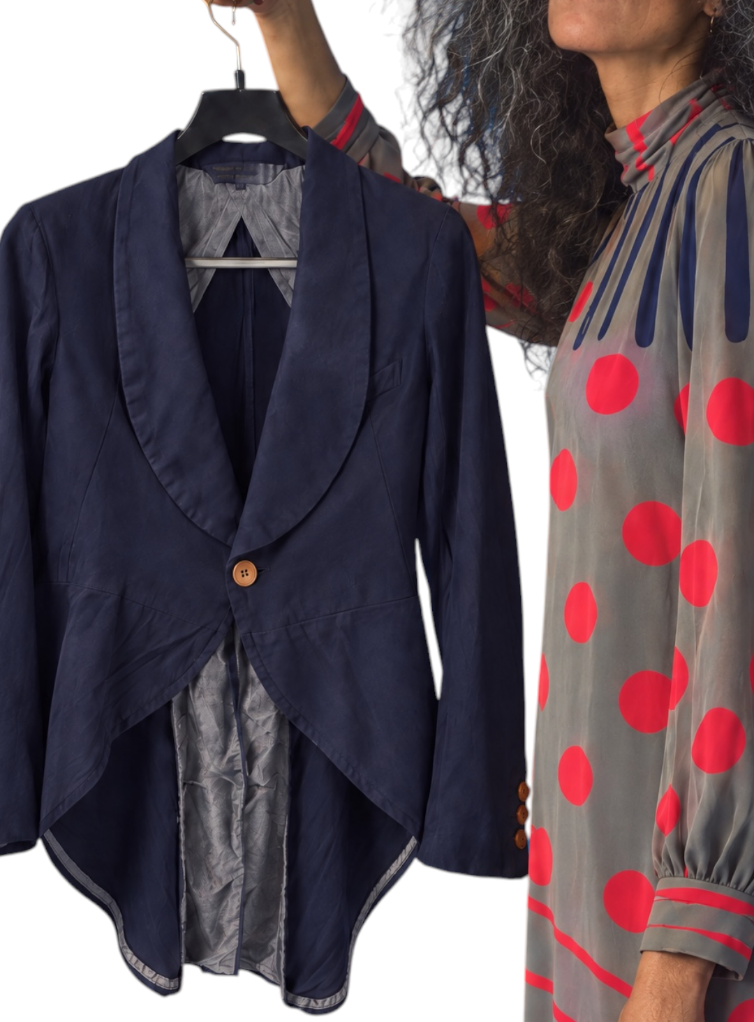 A navy blue asymmetrical draped jacket with a single brown button, shown hanging on a black hanger next to a model wearing a gray dress with red polka dots.