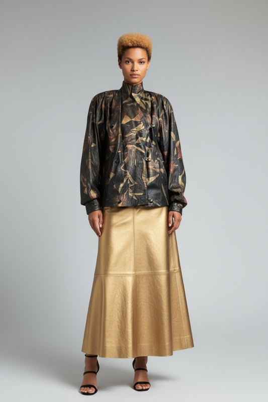 Model wearing a patterned top and gold skirt on a gray background