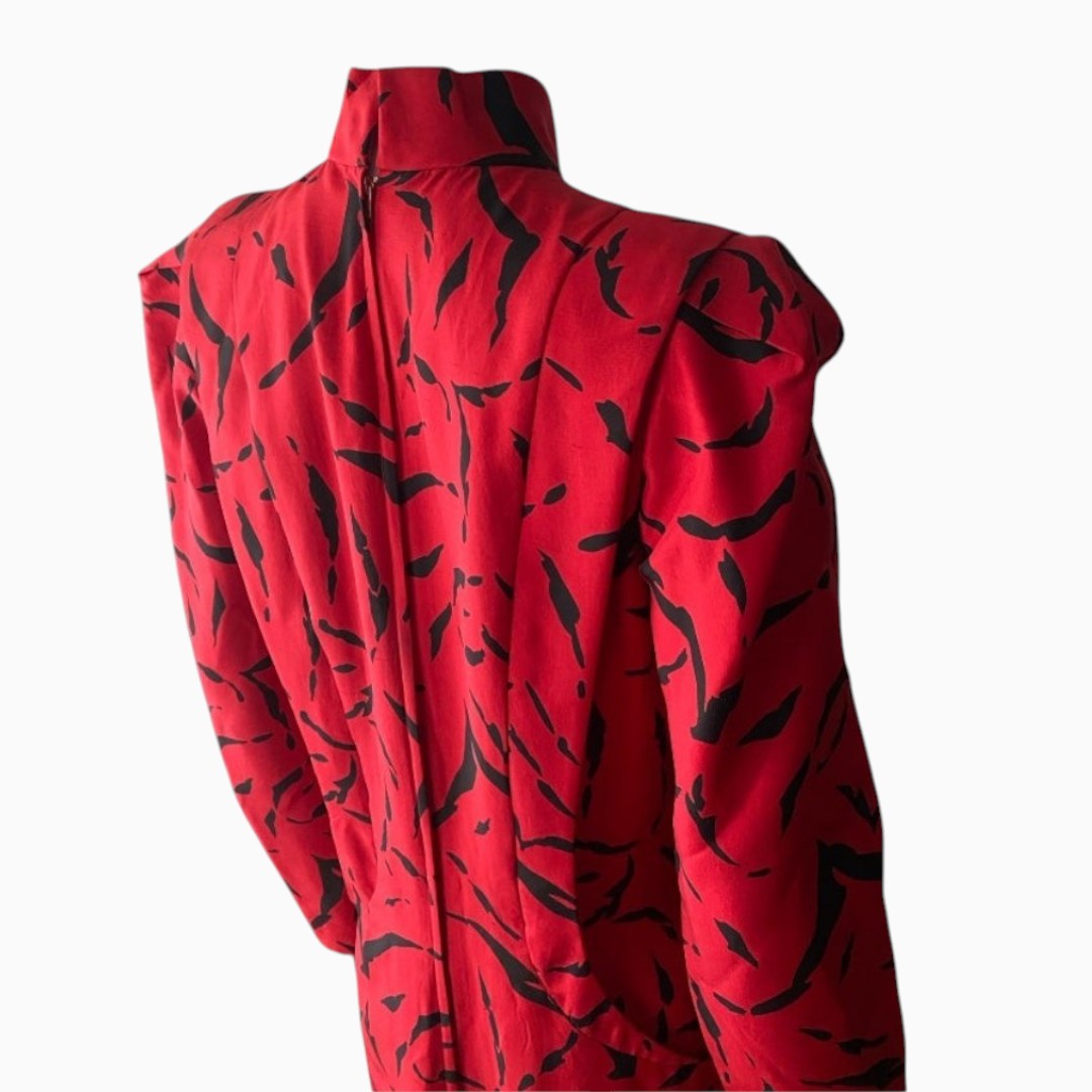 A red long-sleeve top with a black abstract leaf-like pattern, featuring a high mock neck and voluminous puffed shoulders, shown from a three-quarter back angle on a light gray background.