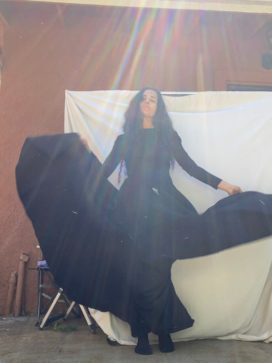 Person wearing a black gown standing on against a wall and white sheet