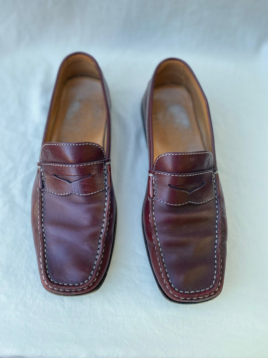 Pair of oxblood leather Tod's penny loafers with white contrast stitching, viewed from above on a white linen background