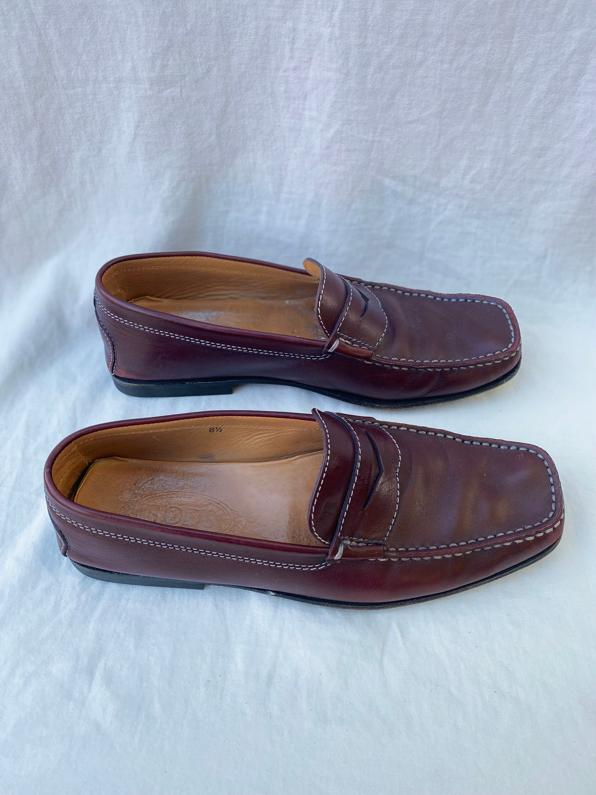 Side view of two oxblood leather Tod's penny loafers showing white stitching and the size 8.5 marking inside