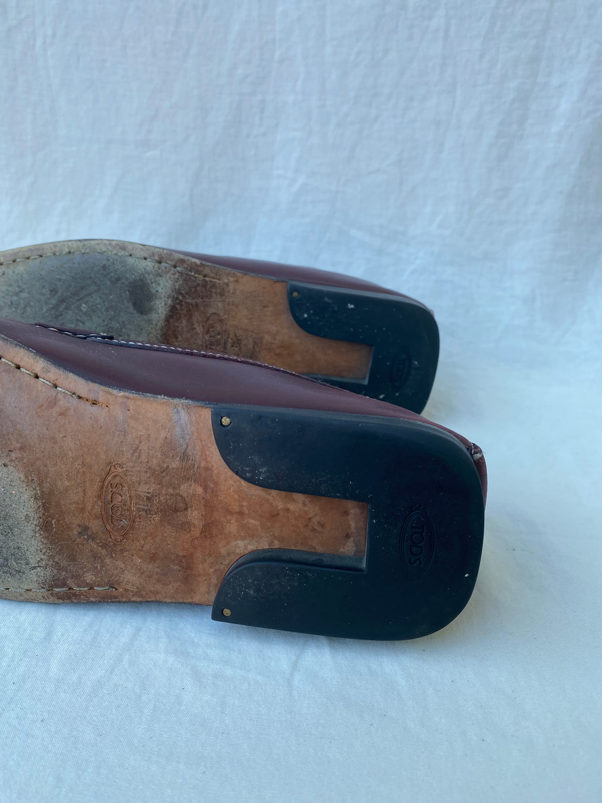 Underside of Tod's loafers showing the Tod's stamped leather sole and black rubber heel pads with brass pins
