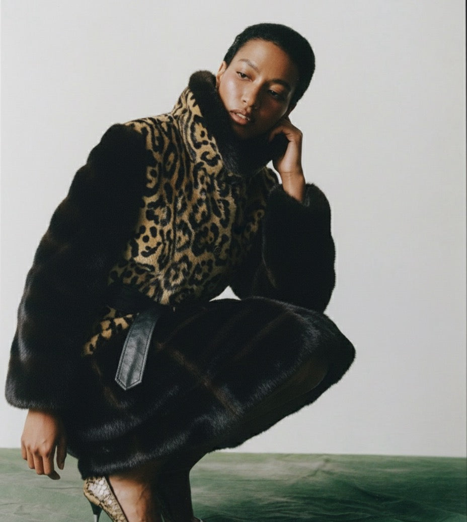 Person wearing a black fur coat with a leopard print scarf against a plain background