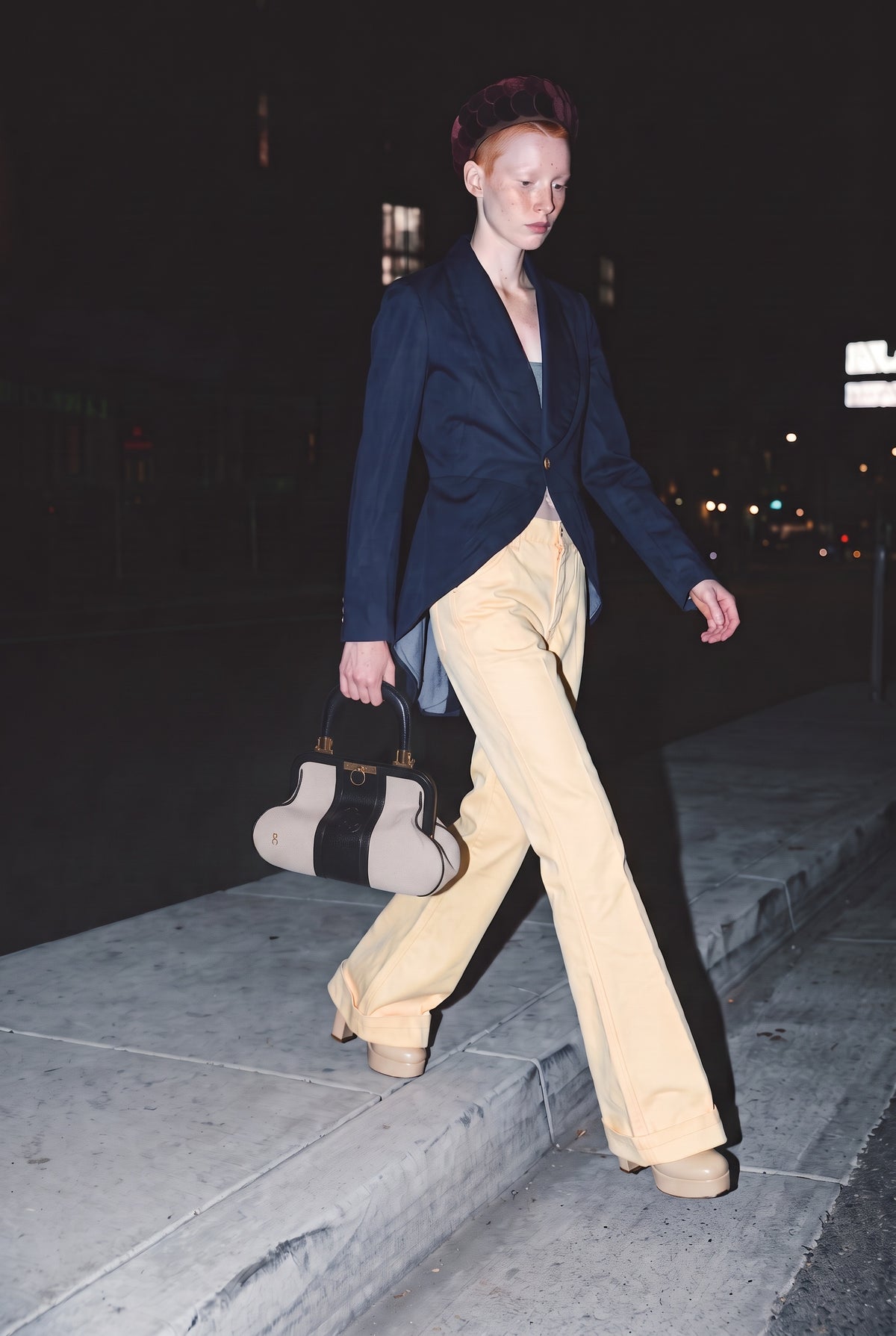Juno wears Comme des Garconne navy blue coat tail Blazer jacket, 1970s men's butter yellow bell bottom pants, holding a Roberta di Camerino canvas doctor's bag