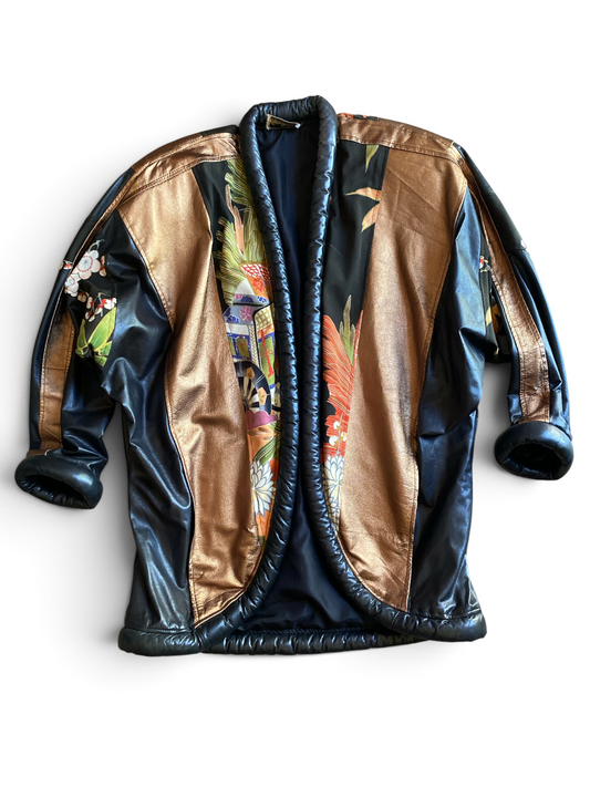 Opulent leather kimono jacket displayed on a dress form, front open, showing the black and bronze leather color-blocking, silk kimono lining panels, and rolled collar