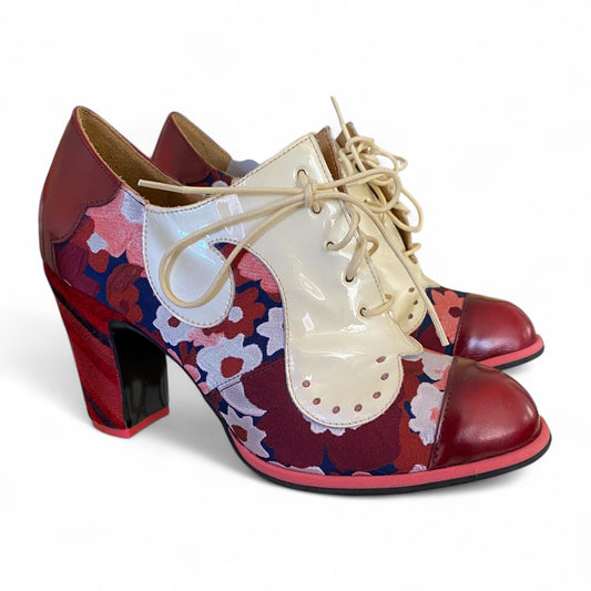 Pair of high-heeled John Fluevog shoes with floral pattern and red base on a white background