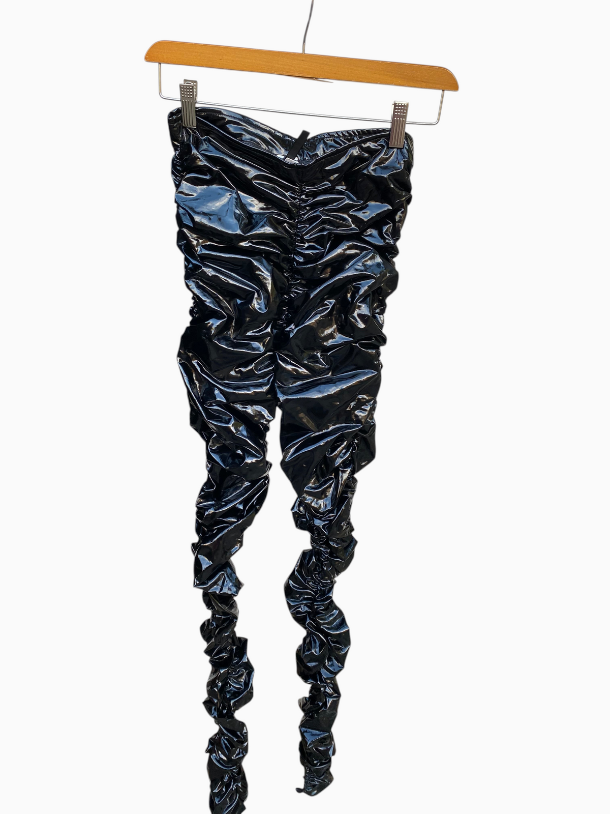 LaliSimone black shiny PU ruched pants with ankle slits hanging on a wooden hanger