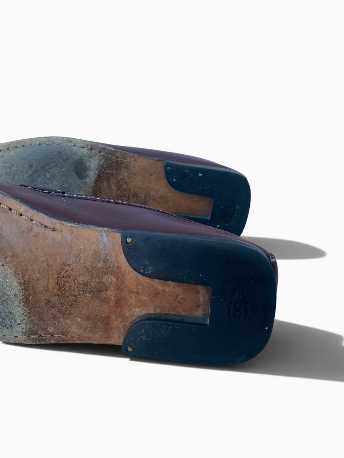 LaliSimone Tod's oxblood leather penny loafers showing the worn leather soles and rubber heel pads from below.
