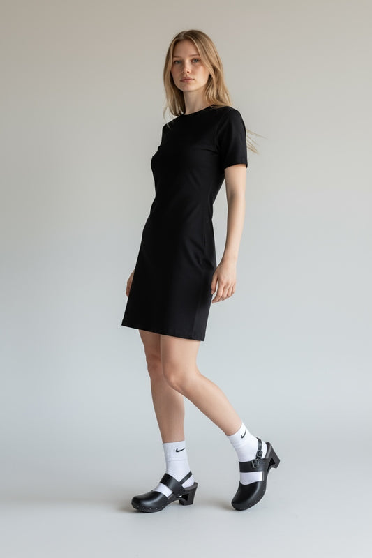Woman wearing a black dress with white socks and black shoes on a plain background